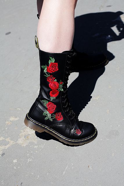 a closeup shot of a black doc martens kneehigh boot with a rose design embroidered on the side, showcasing the footwear's style and detail.