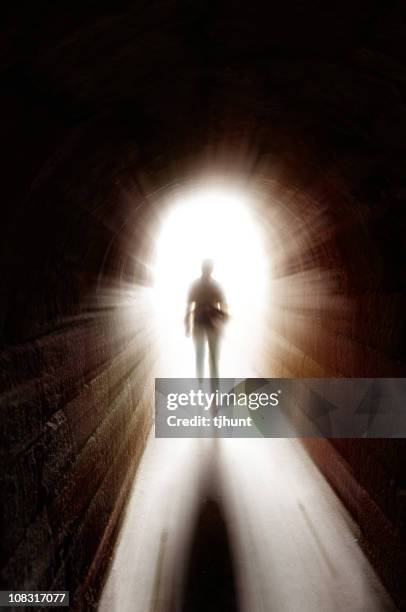 a silhouette of a person walking toward a bright light at the end of a dark tunnel. the light shines down the tunnel, creating a path.
