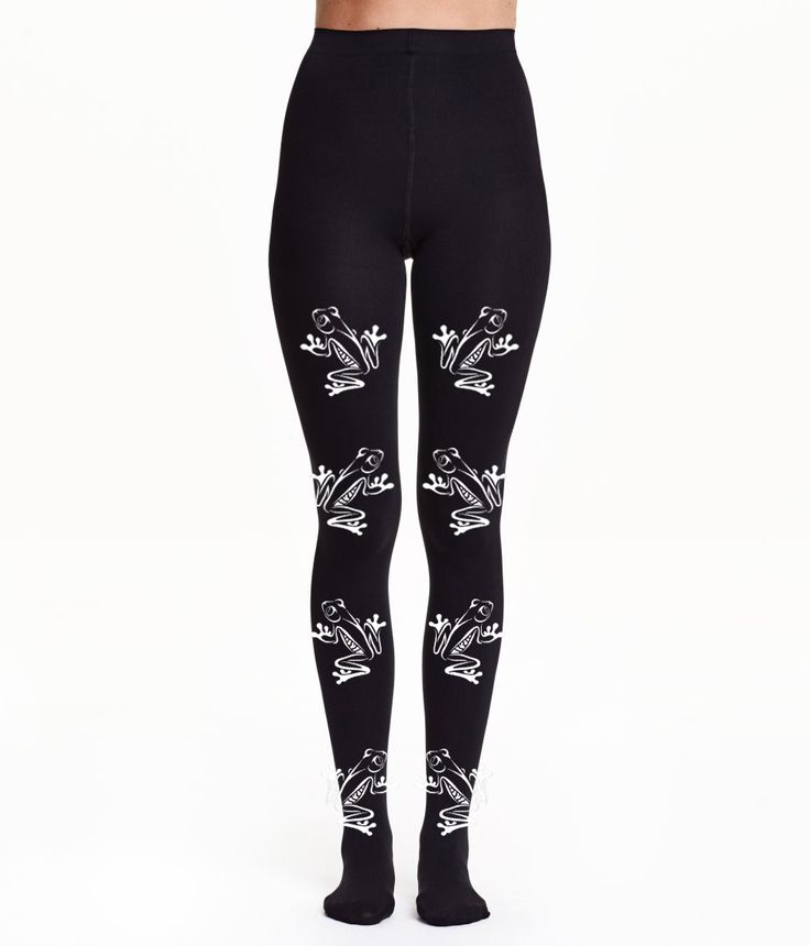 the image shows a pair of black tights with a white frog pattern on the front. the frogs are arranged in pairs, with one frog on each leg. they appear at the top of the tights, around the knees, and near the ankles. the tights are being worn.