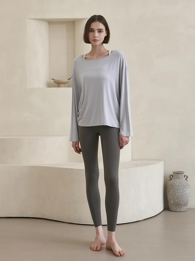 a full shot of a woman modeling a gray long sleeve tshirt and gray leggings while standing barefoot in a studio.