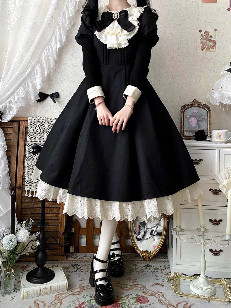 a woman poses in a black and white lolitastyle dress. she is standing in a room with vintageinspired furniture and decor. the dress has a full skirt with lace trim, a white blouse with a ruffled collar and bow tie, and long sleeves with lace cuffs. she is wearing black mary jane shoes and white tights.