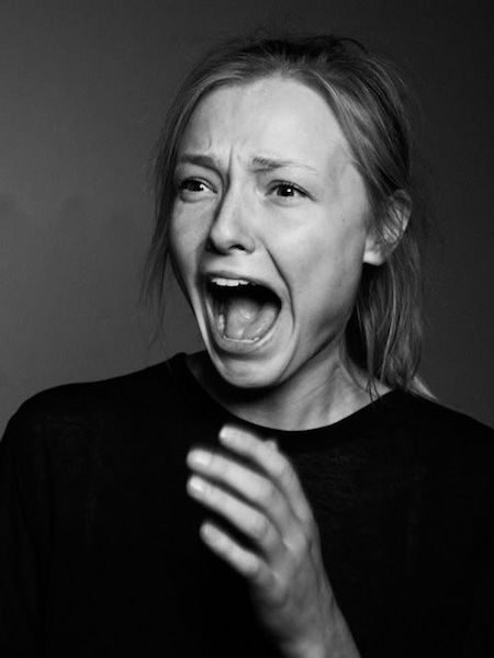 a black and white portrait of a woman with a terrified expression on her face, her mouth open in a scream, her hand raised as if to shield her from something. the image is lit with dramatic lighting, highlighting the woman's features and creating a sense of tension and fear.