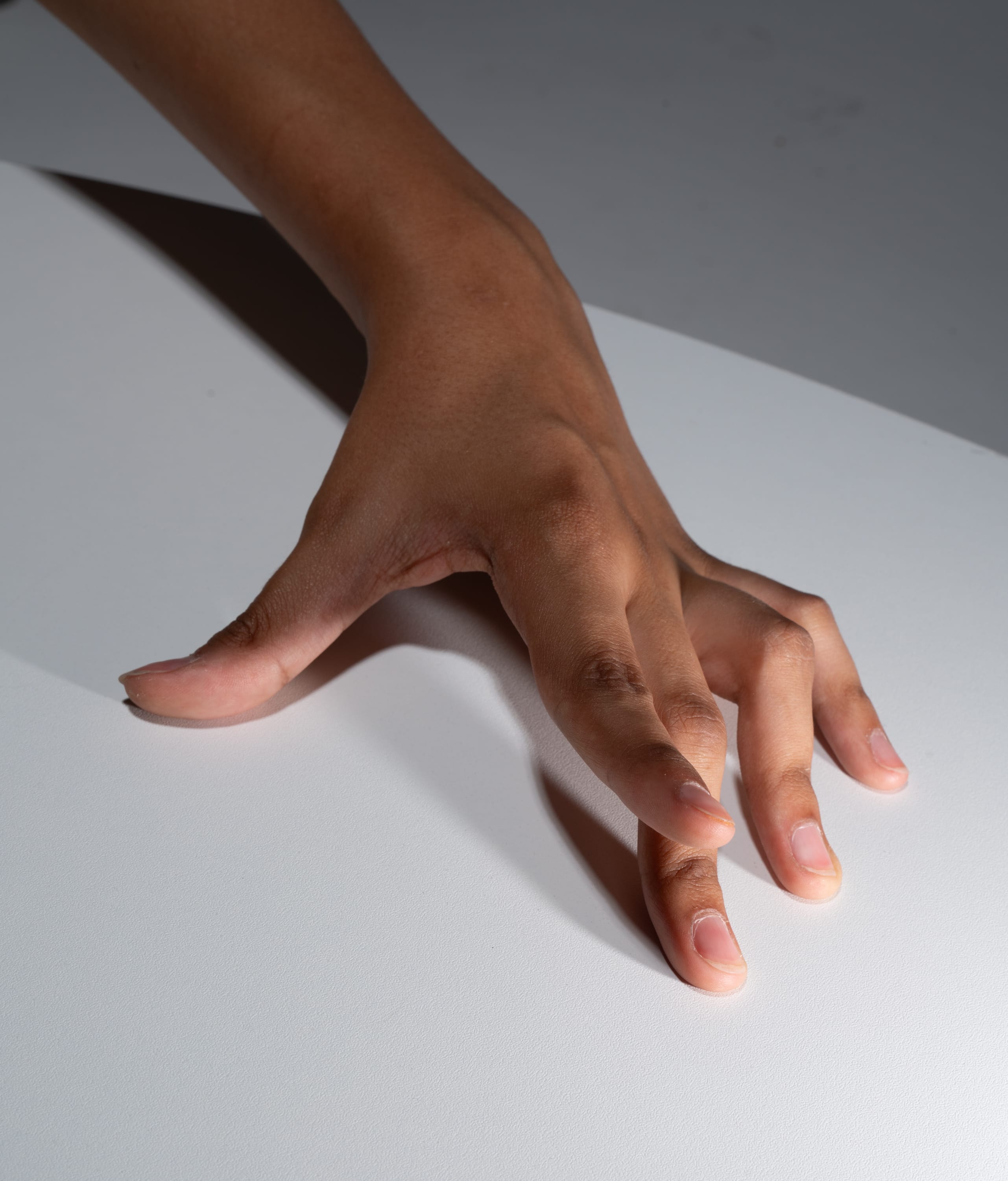 a closeup image of a hand with dark skin resting on a white table. the image is lit by studio lighting.