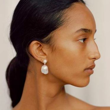 a portrait of a woman wearing pearl earrings, looking away from the camera. her skin is smooth and flawless, and her hair is pulled back to highlight her features. the image is shot from a low angle, and the focus is on her face and the earrings.