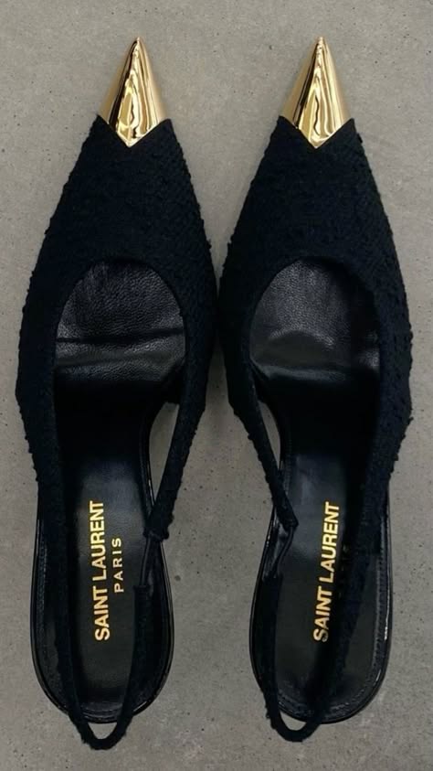 a pair of black high heel shoes with a gold pointed toe. the shoes are by the designer saint laurent and are very elegant. they are perfect for a special occasion or night out.