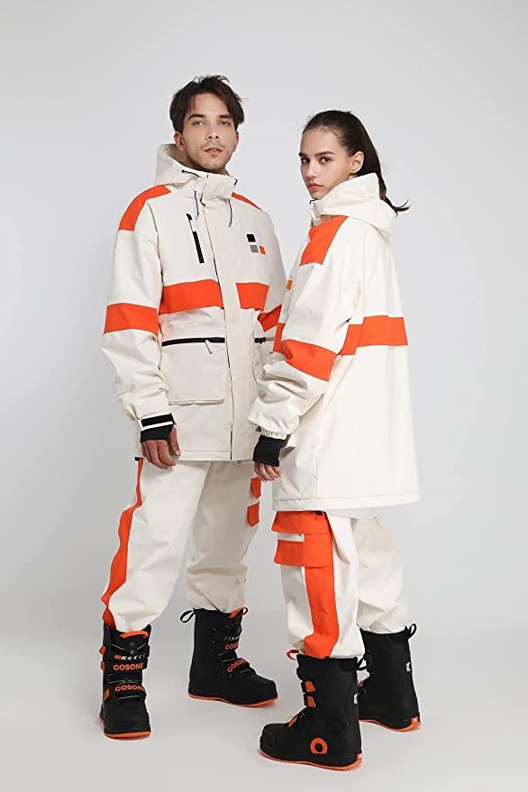 a man and woman wearing matching white and orange ski jackets and pants pose together. both are wearing black ski boots. the man is on the left and the woman is on the right. the background is white.