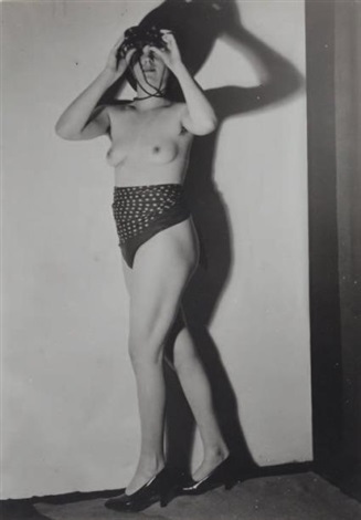 a black and white photograph depicts a nude woman standing against a lightcolored wall.  she is holding binoculars up to her eyes, partially obscuring her face. she wears a polkadot patterned bottom and highheeled shoes. the photograph is notable for its stark contrast, use of shadow, and the subject's pose. the overall aesthetic suggests a vintage or art photography style, possibly from the mid20th century.