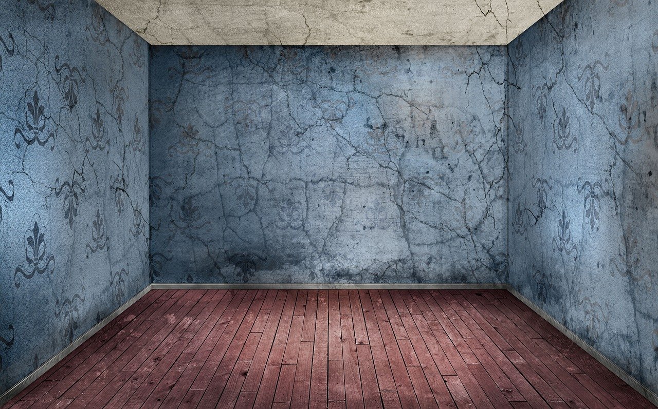 an empty room with blue walls, a patterned wallpaper, and a red wooden floor. the walls have a distressed, cracked look, and the ceiling is concrete.