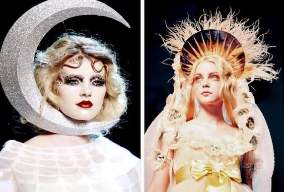 the image shows two female models wearing elaborate headdresses. the model on the left is wearing a silver crescent moon headdress, while the model on the right is wearing a golden sunburst headdress. both models are wearing dramatic makeup and fashionforward clothing.