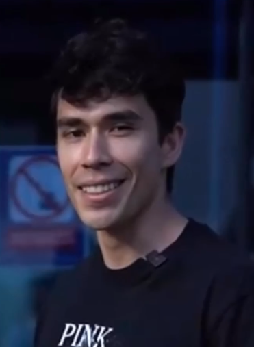a closeup portrait of youtuber and streamer georgenotfound. he is wearing a black tshirt and is smiling at the camera. the image appears to be taken indoors under artificial lighting.