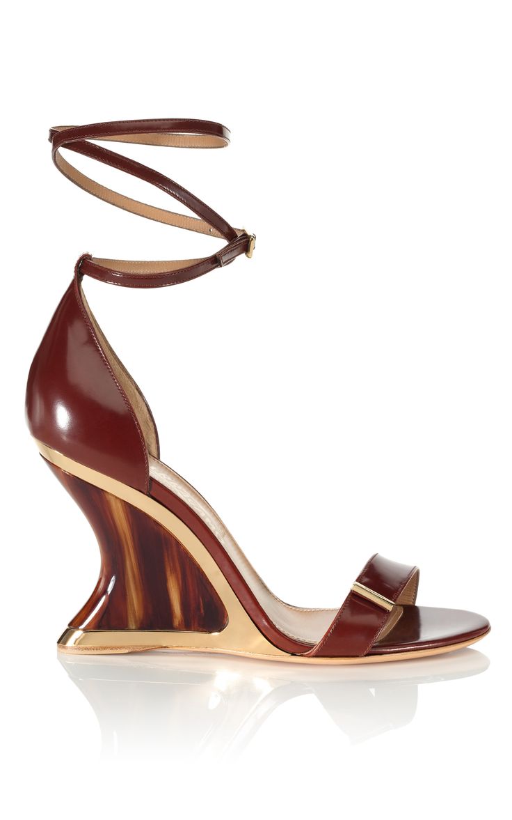 the image shows a pair of women's salvatore ferragamo wedge sandals. the shoes are a rich brown leather with an ankle strap. the wedge heel is made of tortoiseshell material with a gold accent at the bottom. the shoes are elegant and stylish and suitable for formal occasions or parties. the background is white, and the shoes are displayed on a reflective surface.