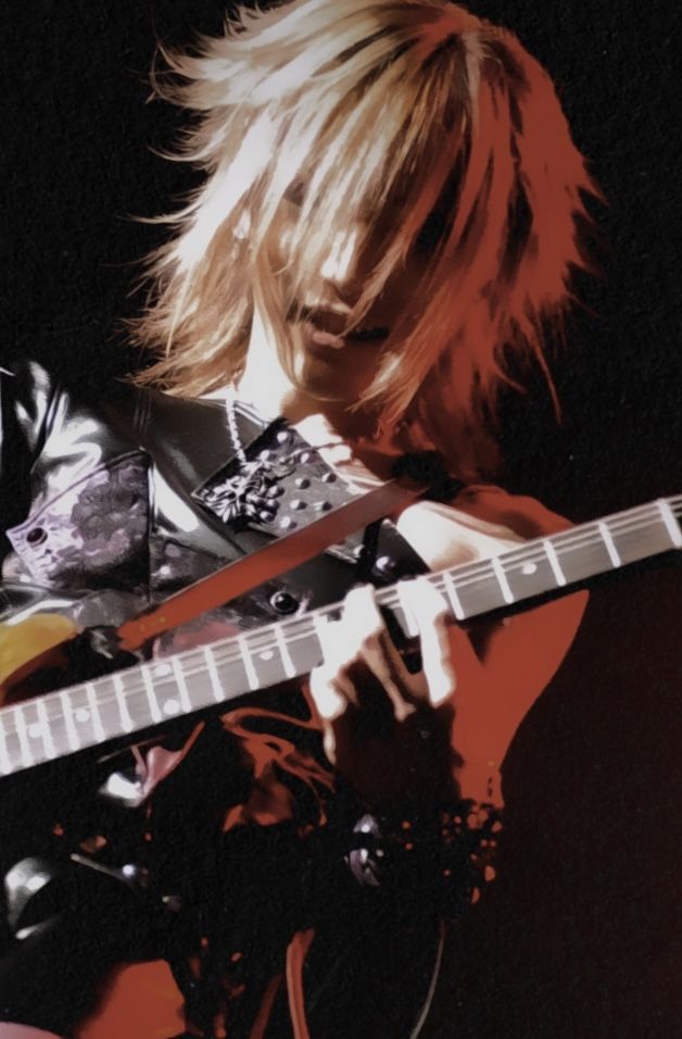 a closeup shot of a male musician playing a red electric guitar on stage. the musician's blonde hair is long and flowing, and he has a focused look on his face as he plays. he is wearing a black leather jacket and has a dark background behind him. the image is dramatic and intense, capturing the passion and energy of the musician's performance.  the image is focused on the musician's head and shoulders, and there is a slight blur to the background.  this image is reminiscent of a rockstar in a concert.
