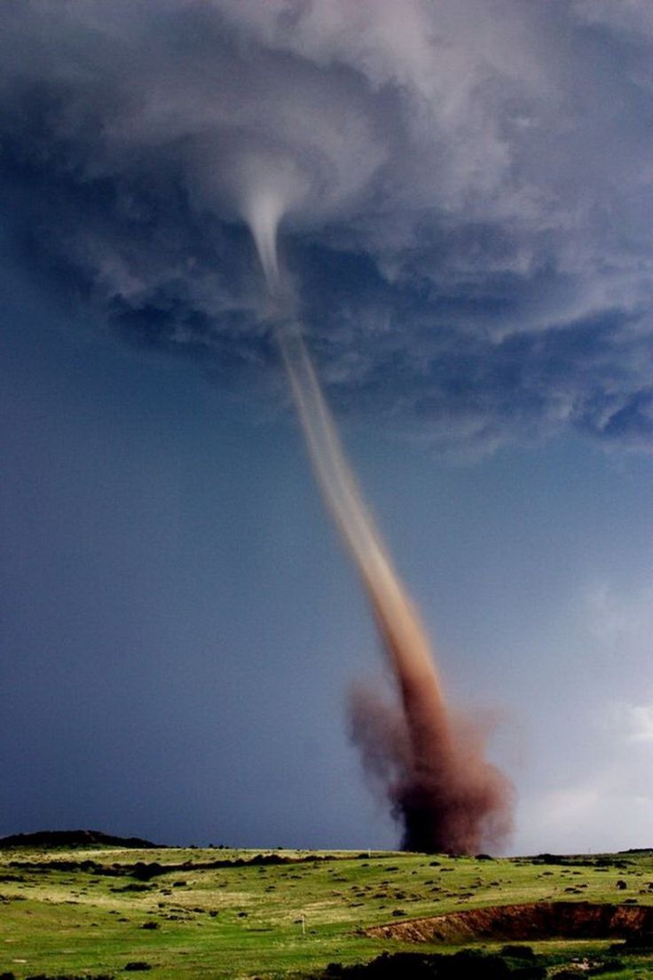 a powerful tornado touches down in a field, creating a swirling vortex of dust and debris. the funnel cloud is dark and ominous, extending down from a stormy sky filled with dark clouds. the field is green and grassy, with the tornado's destructive force clearly visible. the image captures the raw power and danger of nature's fury.