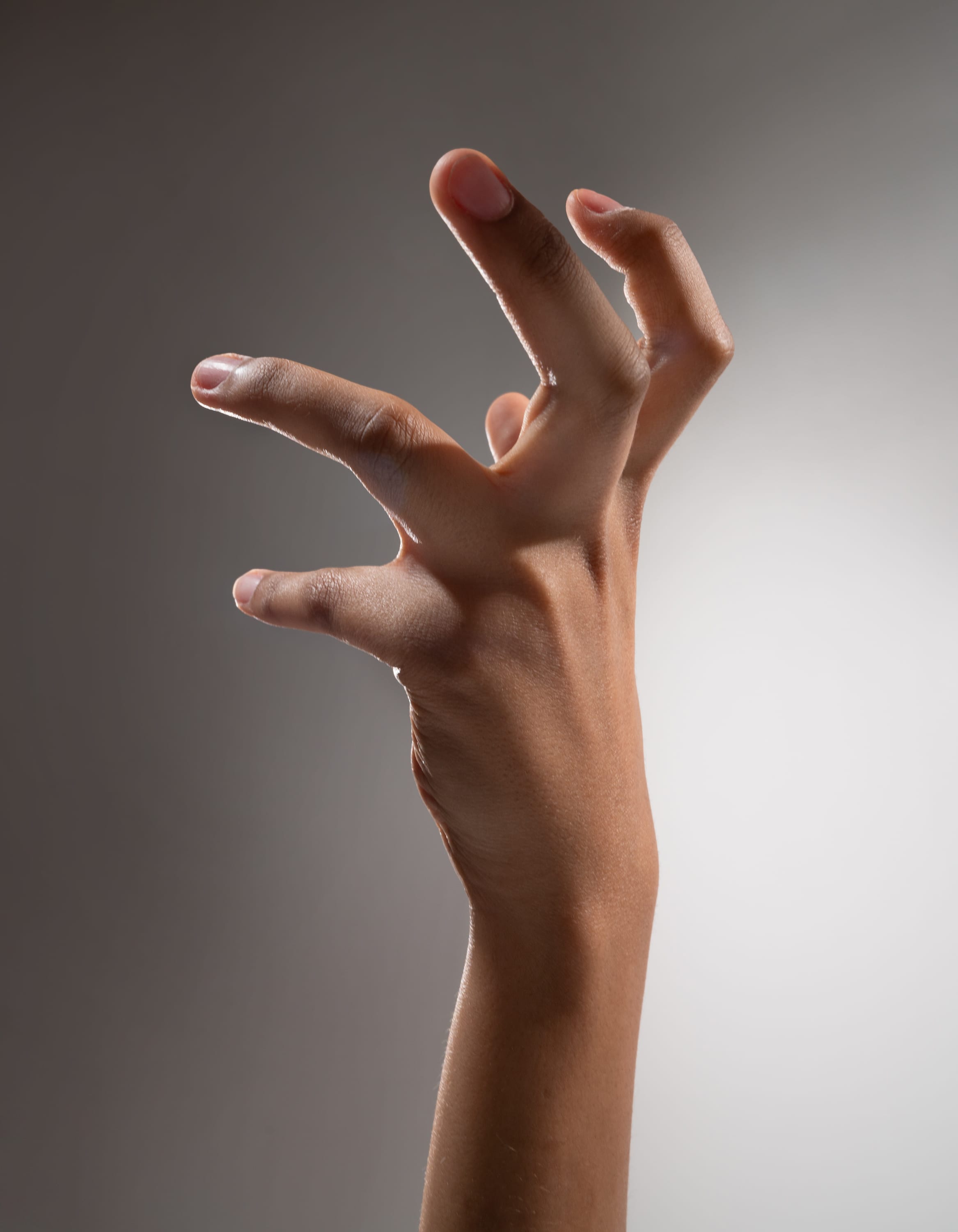 a single hand is extended upward with the fingers curled in a clawlike gesture against a grey background. the hand appears tense, as if reaching or grasping for something.