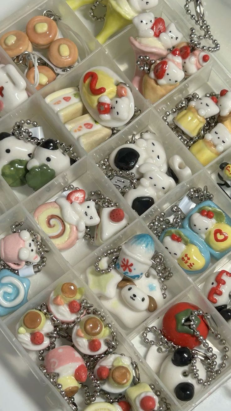 a closeup overhead shot showcases a collection of handmade, miniature polymer clay keychains arranged in a clear plastic compartmentalized case. the keychains feature various kawaiistyle designs including animals (like pandas, dogs, bears, rabbits), assorted foods (pancakes, cakes, sushi, ice cream), and other themed charms. each keychain is attached to a metal chain and is intended as an accessory for bags, keys or other items. the composition suggests a wide variety of handcrafted, collectible trinkets for personal use or as gifts.