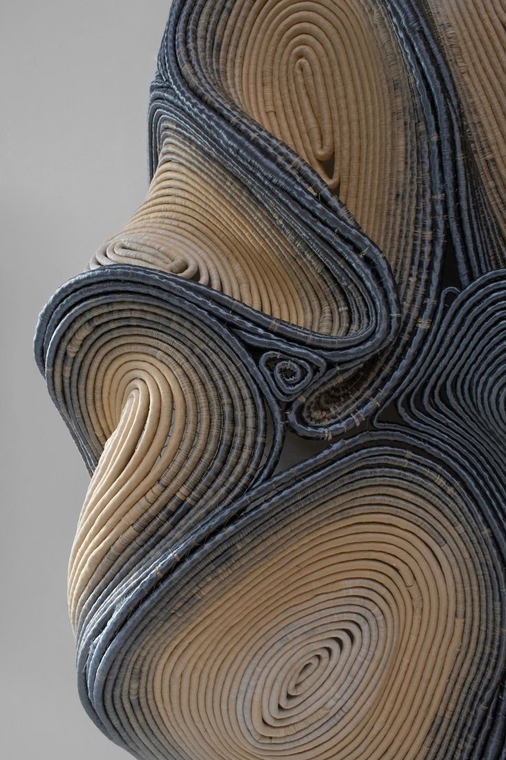 a closeup view of a contemporary sculpture with a swirling and dynamic form made from stacked layers of woven material. the sculpture is crafted from layers of brown and blue material, creating a complex and captivating texture. the closeup shot highlights the intricate details of the sculpture, showcasing the way the material is woven and coiled to create a threedimensional form. the sculpture's organic shape is both abstract and visually engaging, suggesting a sense of movement and energy. the overall effect is one of complexity and sophistication, making this sculpture a powerful piece of contemporary art.