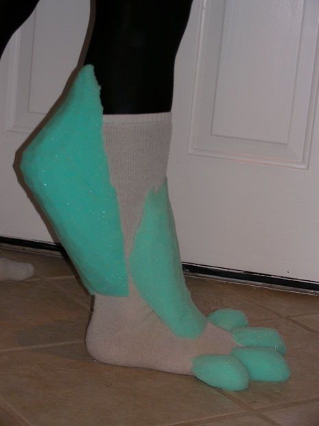 a closeup image of a person's foot wearing a furry costume paw, that looks like a green hand with toes, on their foot.