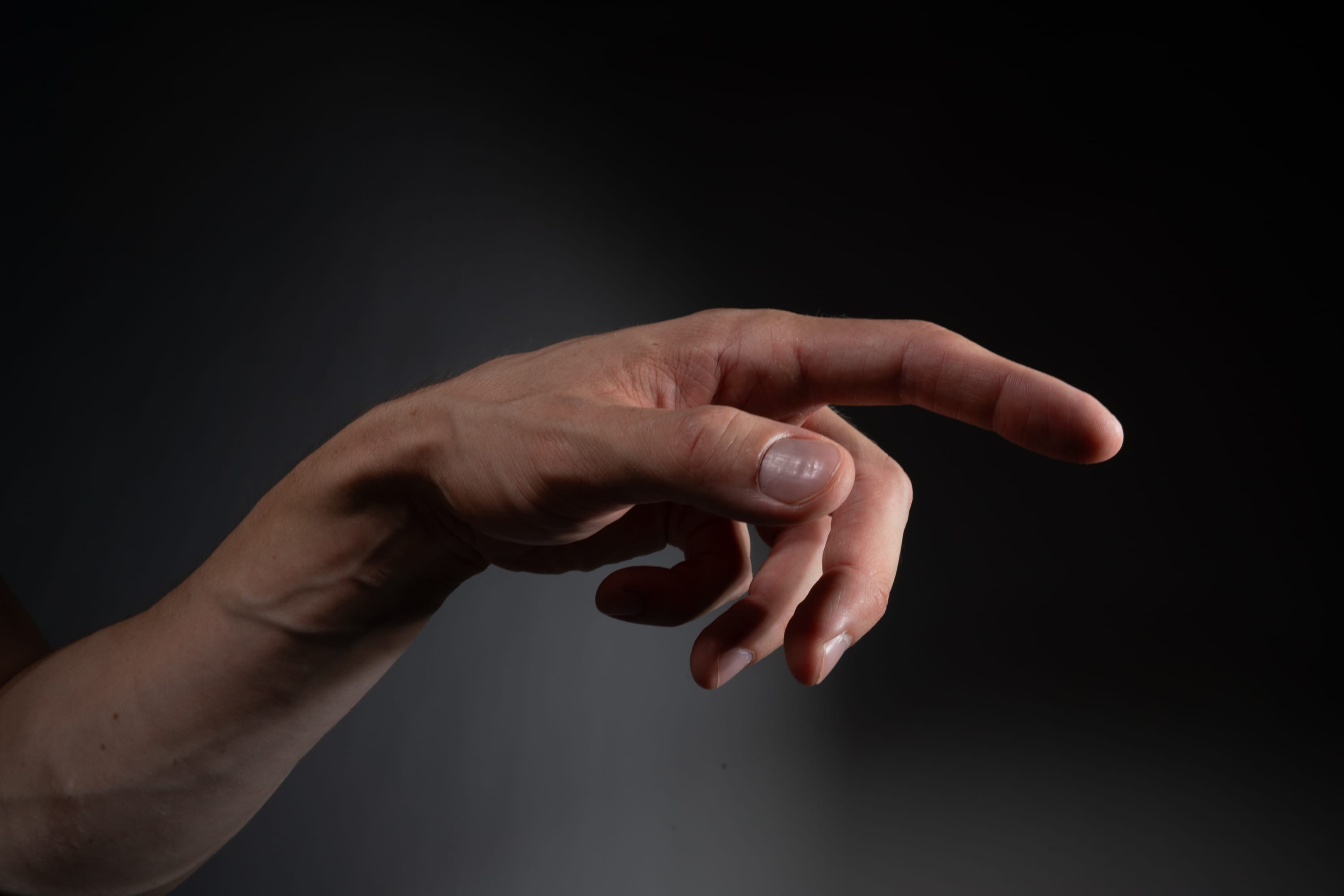 a right hand against a dark background pointing with the index finger to the right of the image.