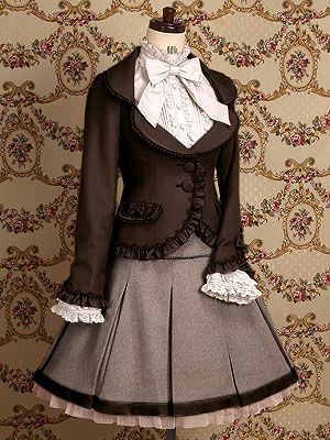 a brown and cream lolita fashion outfit displayed on a mannequin. the outfit consists of a brown jacket with ruffled trim, a white blouse with a lace jabot and bow, and a brown skirt with brown velvet trim. the background is a floral wallpaper in shades of brown and cream. the lighting is soft, giving the image a vintage feel.
