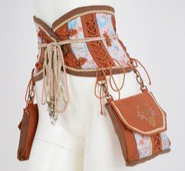 a corset belt with a brown and floral pattern is displayed on a mannequin. the belt features laceup detailing and decorative strings. attached to the belt is a brown purse or pouch with a floral pattern on the flap. the overall style appears to be handmade or steampunkinspired.