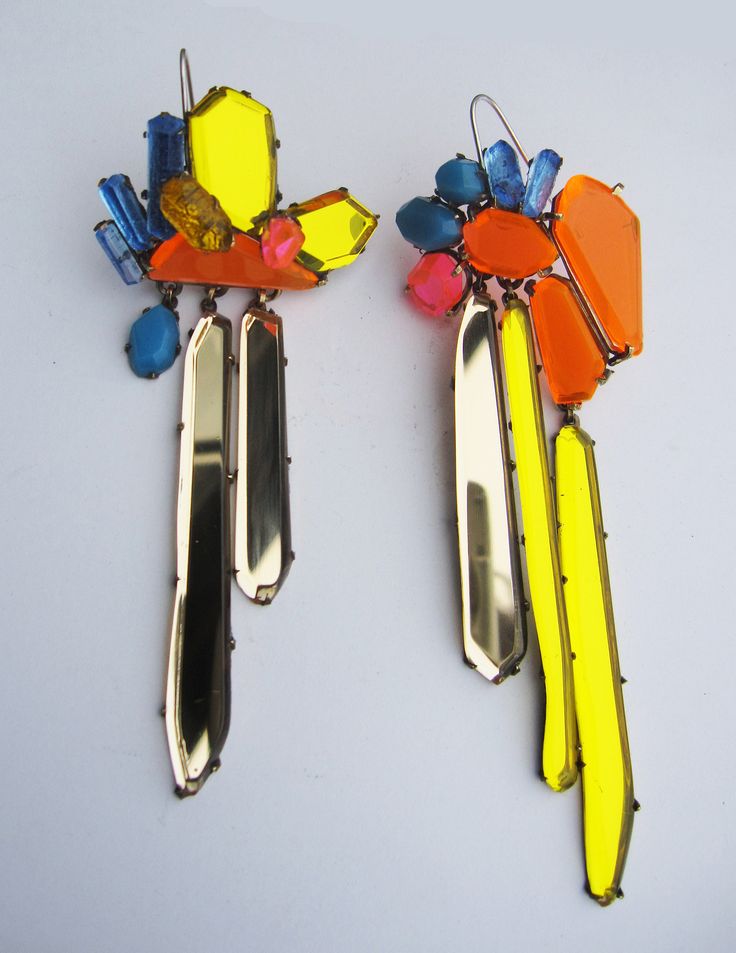 the image shows a pair of vibrant, asymmetrical earrings.  each earring features a cluster of faceted acrylic stones in bright neon yellow, orange, pink, and blue, arranged seemingly organically.  these clusters are attached to several elongated, polished metallic (goldcolored) pieces that hang down, creating a cascading effect. the overall style is contemporary and bold, showcasing a mix of bright colors and reflective metallic elements.  the earrings are displayed against a simple white background, which emphasizes their striking colors and design.