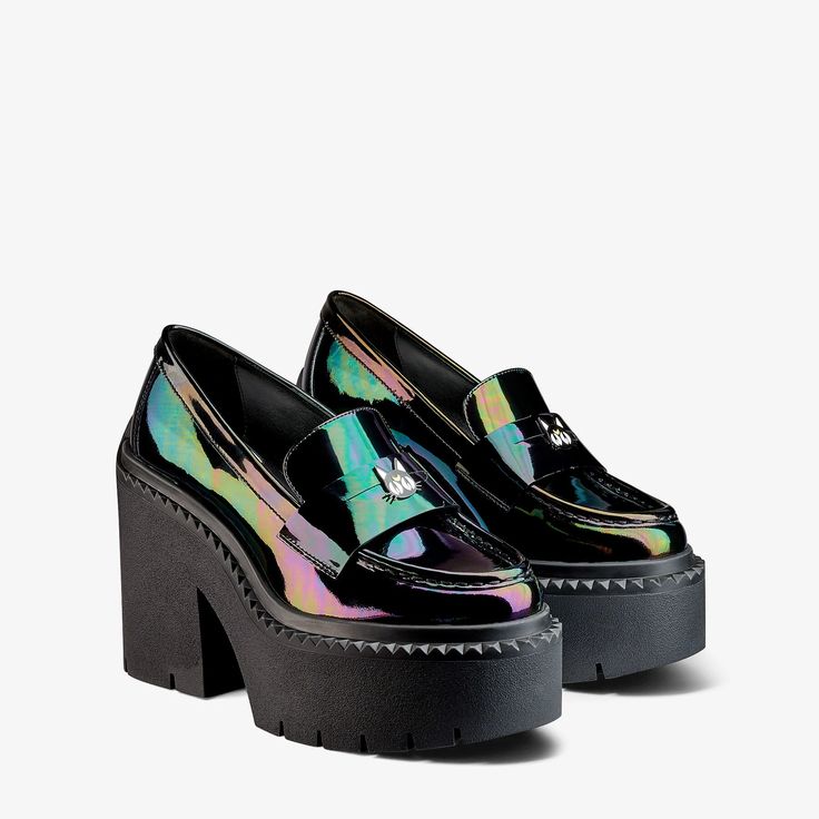 a pair of black iridescent platform loafers are displayed on a white background. the shoes feature a shiny finish with rainbowlike reflections, chunky heels, and platform soles with a textured edge. a small catshaped decoration is visible on the upper part of the left shoe.