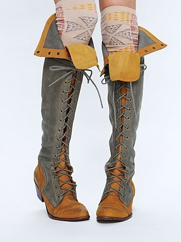 a frontfacing view shows a pair of laceup boots extending from the ankles to just below the knees. they are laced with gray strings and have a unique twotone color scheme: a tan hue at the toes and ankles, transitioning to a light gray for the rest of the boot's height. both boots have cuffs at the top, adding to their distinctive look. above the boots, patterned socks peek out, suggesting the wearer is covering their legs with both the boots and the socks.