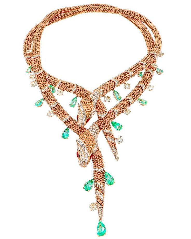 the image shows a detailed and elaborate necklace featuring two snake designs intertwined. the necklace is primarily gold in color and adorned with numerous diamonds and emeralds. the snakes have red gemstones for eyes and are encrusted with diamonds on their heads. the necklace appears to be a luxurious and expensive piece of jewelry, likely a high fashion statement piece.