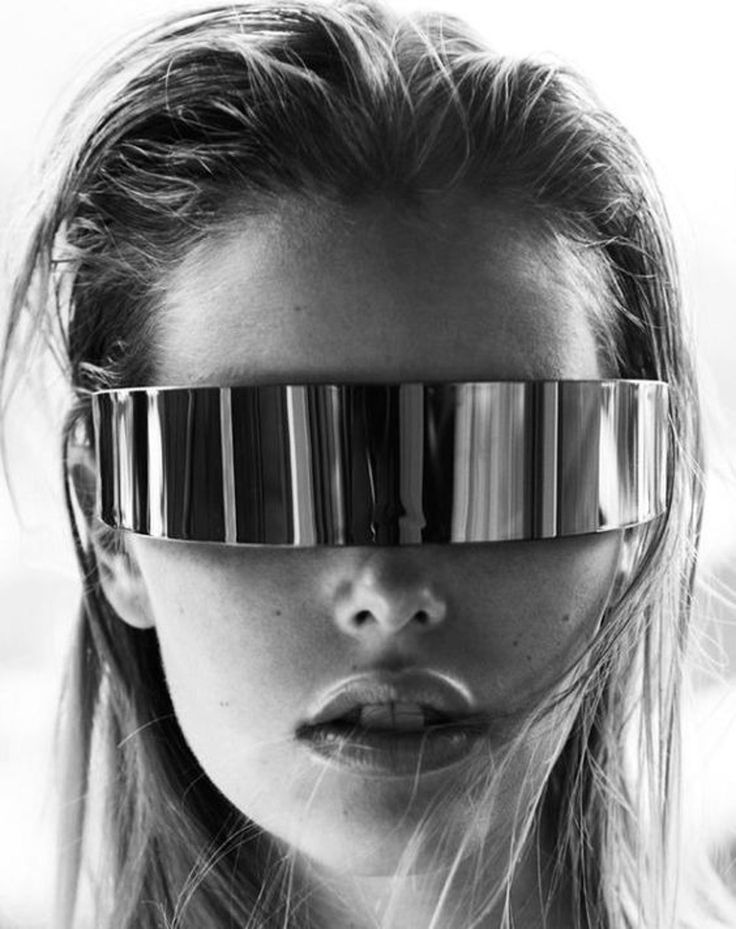 a black and white closeup portrait of a woman's face.  her long hair cascades around her shoulders. she is wearing a futuristic, silver, reflective visorstyle pair of sunglasses that covers her entire brow and extends across her eyes. the sunglasses are metallic and feature vertical lines, reflecting light. the woman's expression is serious and her lips are slightly parted. the overall aesthetic is fashionforward, edgy, and futuristic. the background is blurred and outoffocus, drawing all attention to the model.