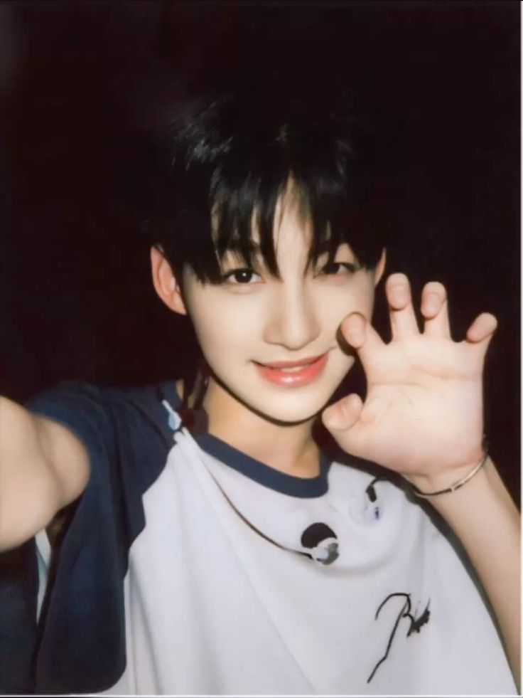a young asian man with black hair is smiling with a hand up to his face. he is wearing a white and black shirt. the image is slightly grainy, which gives it a vintage aesthetic.