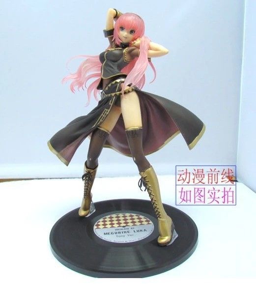 a megurine luka vocaloid anime figure stands on a black record base. she has pink hair and is wearing a black dress with gold accents and gold laceup boots. she is posed with one hand on her head and the other outstretched.