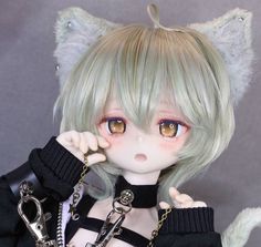 a closeup portrait of a balljointed doll with blonde hair and cat ears. the doll is wearing a black outfit and has large, expressive eyes. it appears to be in a studio setting with soft lighting.