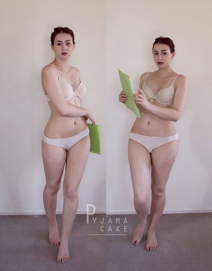 a woman is standing in front of a white wall. she is wearing a white bra and matching panty. she is holding a green book in her right hand. she is looking at the camera.  she is wearing a slight smile.