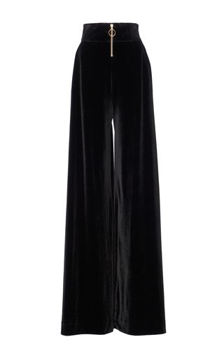 a pair of black velvet wideleg pants with a high waist and a gold zipper fly. the pants are long and flowy, and they have a relaxed fit. the fabric is soft and luxurious, and the pants are perfect for dressing up or down.