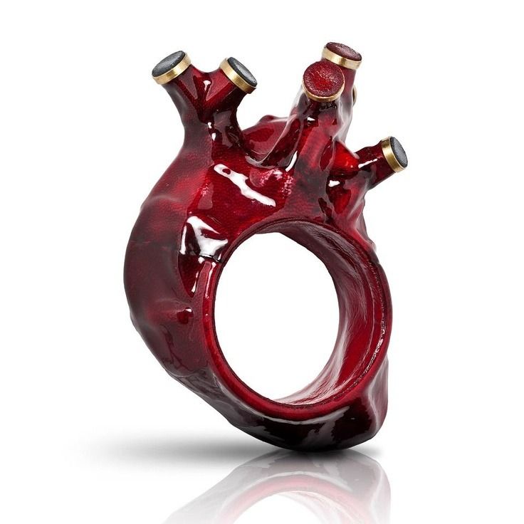 a closeup shot of a unique red heart ring. the ring is made of a sculpted heart shape with intricate details and a glossy finish. it is a statement piece that is both bold and beautiful. the ring is set against a white background, which helps to highlight its vibrant color and intricate details.