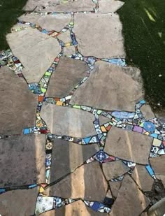 a closeup shot of a mosaic stone pathway made of various colorful tiles. the walkway is outdoors and surrounded by green foliage. the tiles are arranged in a random pattern, creating a visually interesting and textured surface. the pathway is wellmaintained and looks like a beautiful and unique addition to the garden.