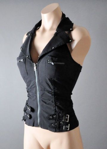 a woman is posing in a black halter top with a zipper down the front and buckles on the straps. she is standing in front of a grey background. the top is sleeveless and the woman is wearing a neutral expression.