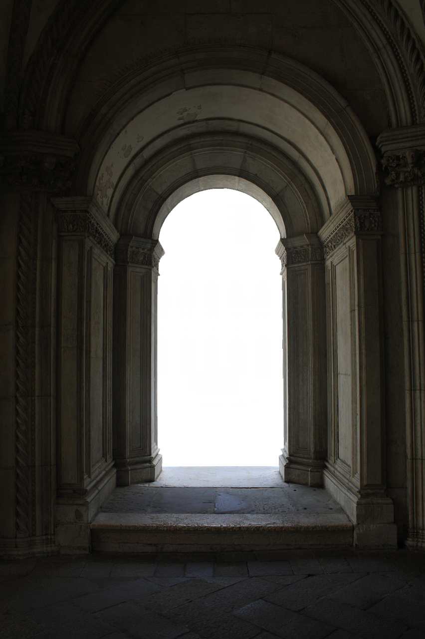 a photograph of an arched doorway in an old stone building. the archway is tall and has intricate details around the edges. the doorway leads to a black space. the building appears to be made of stone and is dark, with the light coming from somewhere behind the viewer.