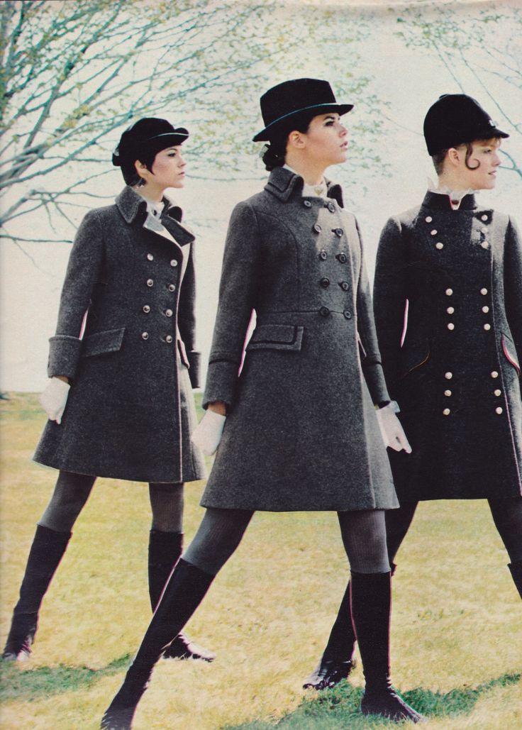 three women in vintage fashion are walking outdoors. they are all wearing coats, hats, gloves, and boots. the coats are doublebreasted and gray. the photo has an autumn aesthetic.