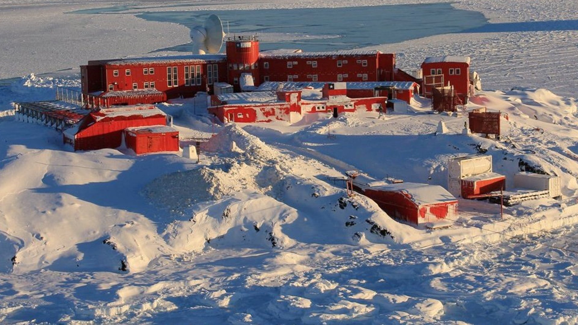 a wide shot of a red research station in antarctica, nestled amidst a snowy landscape. the station consists of a cluster of buildings, connected by walkways and surrounded by snowcovered mountains. the buildings are red in color, contrasting sharply with the white snow and ice. the scene is desolate and remote, giving a sense of the harsh conditions that researchers face in antarctica. the photo captures the beauty and grandeur of this frozen landscape.