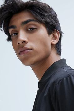 a young man with dark hair and brown eyes is posing in a studio. he is wearing a black bomber jacket and looking directly at the camera. the lighting is soft and highlights his facial features.
