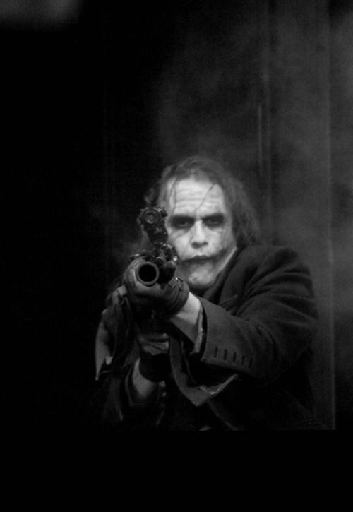 a black and white portrait of a man with an intense look on his face holding a gun, with a dark and mysterious background. the man is likely a character from a comic book or movie, potentially the joker from batman.  he is a villain, and the image captures a moment of action, tension, and threat.