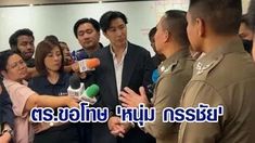 a man in a black suit is surrounded by people holding microphones and cameras. a police officer stands to his right. the image appears to be from a news interview.