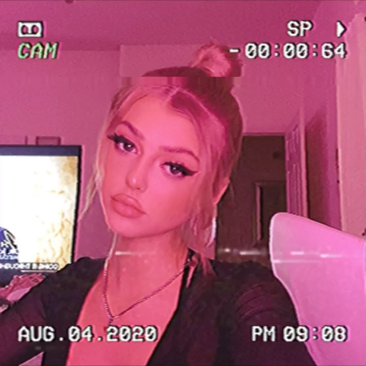 a pinktinted image of a woman, filtered to look like it was recorded on a vhs camcorder. the woman has blonde hair pulled back in a bun, wears makeup, and has a necklace. a vhs timestamp can be seen on the image. the date is august 04, 2020.