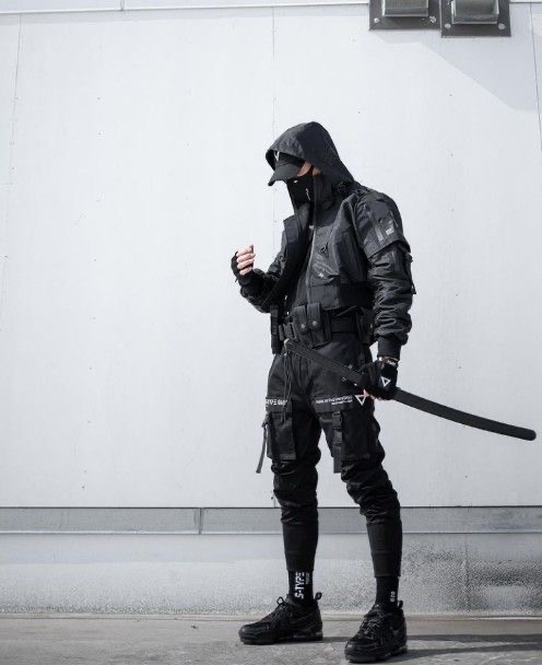 a man in a black hooded jacket and pants, with a sword strapped to his back, standing against a white wall. he is wearing black boots, and a black face mask. he is looking off to the side.  his style is cyberpunk and urban.