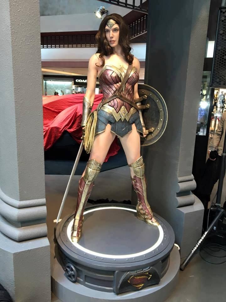 a wonder woman statue stands on a display platform in a store, showcasing the iconic superheroine. she is posed in a fierce and powerful stance, holding her sword and shield, ready for battle. her costume, with its signature red, blue, and gold accents, is meticulously detailed. the statue is a lifelike representation of the character, capturing her strength and determination. the display platform features a superman logo, hinting at the shared universe these characters inhabit.