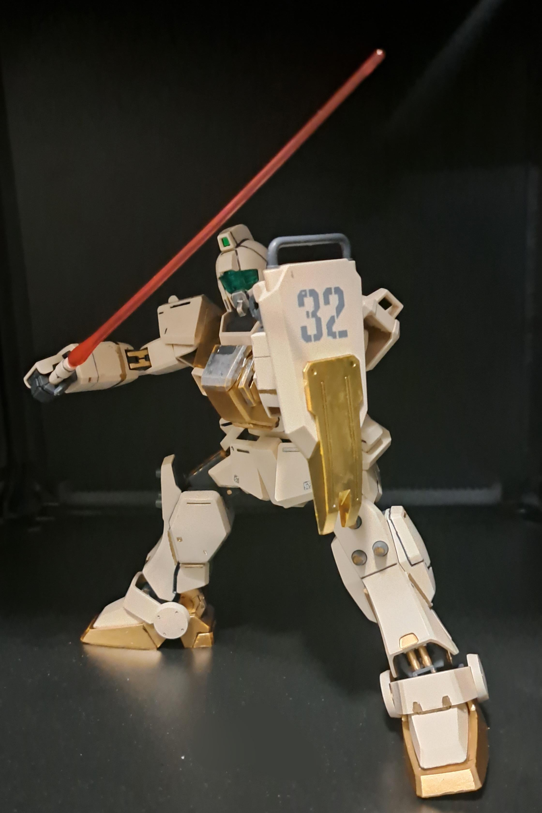a plastic model kit of the rx782 gundam from the anime series mobile suit gundam, posed in a dynamic stance and wielding a beam saber. the model is painted in a custom color scheme of white, gold, and green.