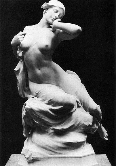 a black and white photograph shows a nude white statue of a woman seated upon drapery. the woman reclines slightly, with one arm raised to her face as if resting, and the other arm slightly extended with a hand near her chest. her head is turned to the side and she wears a head covering. the statue is mounted on a base.