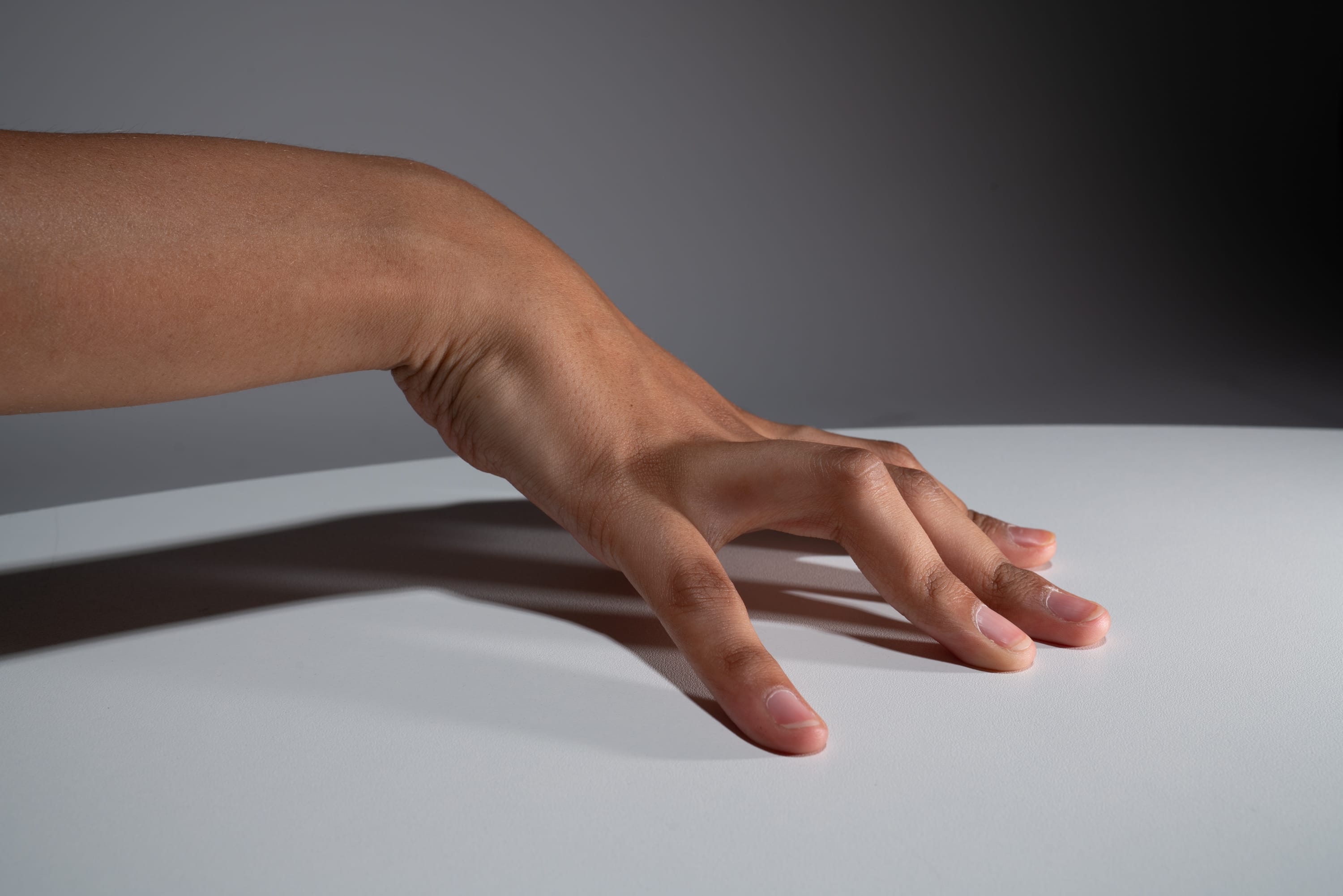 a closeup shot of a hand with dark complexion gently resting on a white table surface. the hand is outstretched, fingers slightly curled, casting a soft shadow under the studio lighting. the image highlights the details of the skin texture and the natural curvature of the hand.