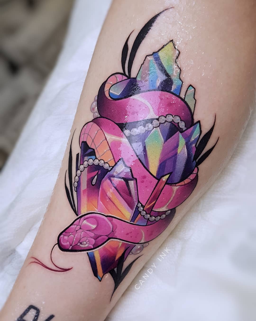 a tattoo on someone's forearm of a pink snake wrapping around a cluster of rainbow crystals.